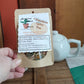 Cinnamon spice loose tea in eco kraft package held by a hand with a teapot in the background