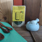 Packaged poultry seasoning in kraft window bag on a wooden surface with a green cloth and wooden spoons.