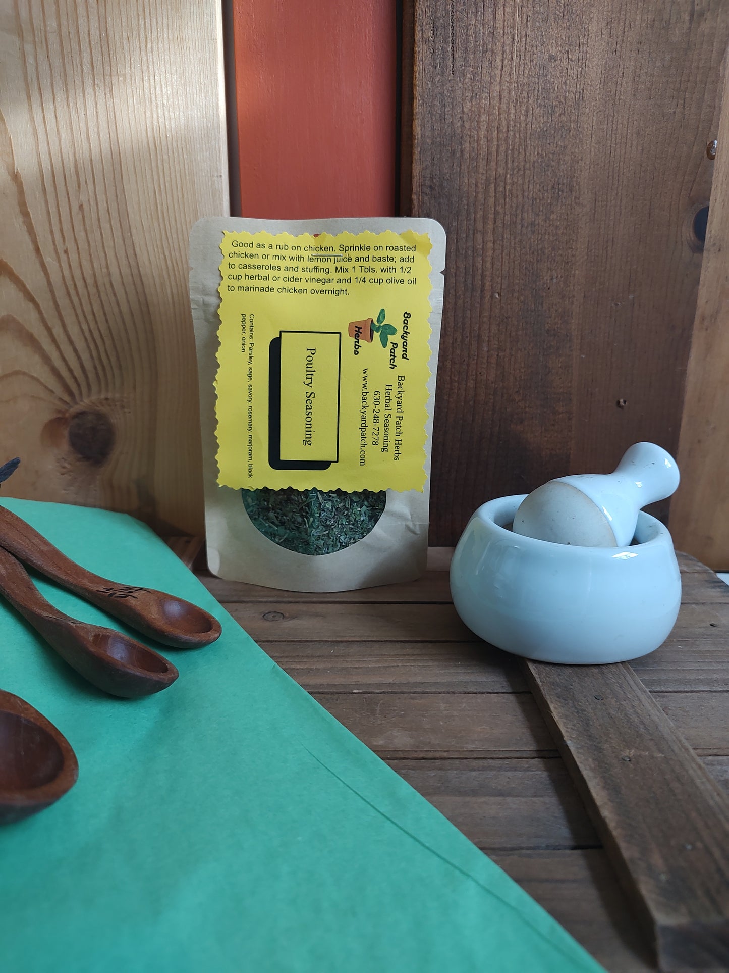Packaged poultry seasoning in kraft window bag on a wooden surface with a green cloth and wooden spoons.