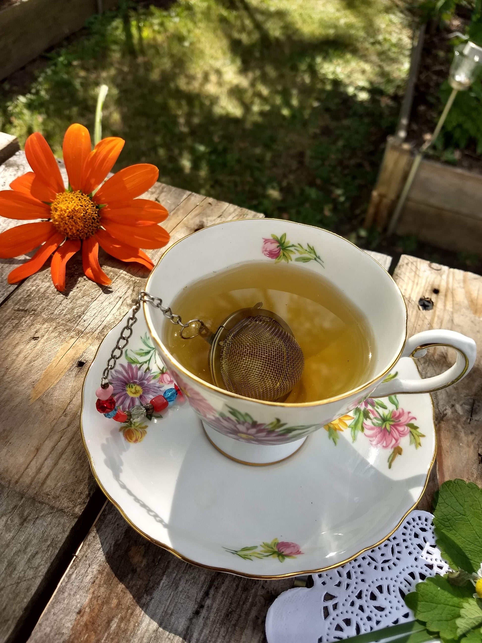 floral tea cup with brewed gold colored rest easy tea and a tea ball