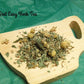 Loose Rest Easy Tea in a pile on wood tea cup containing chamomile, lemon balm, catnip, spearmint and lemon grass 