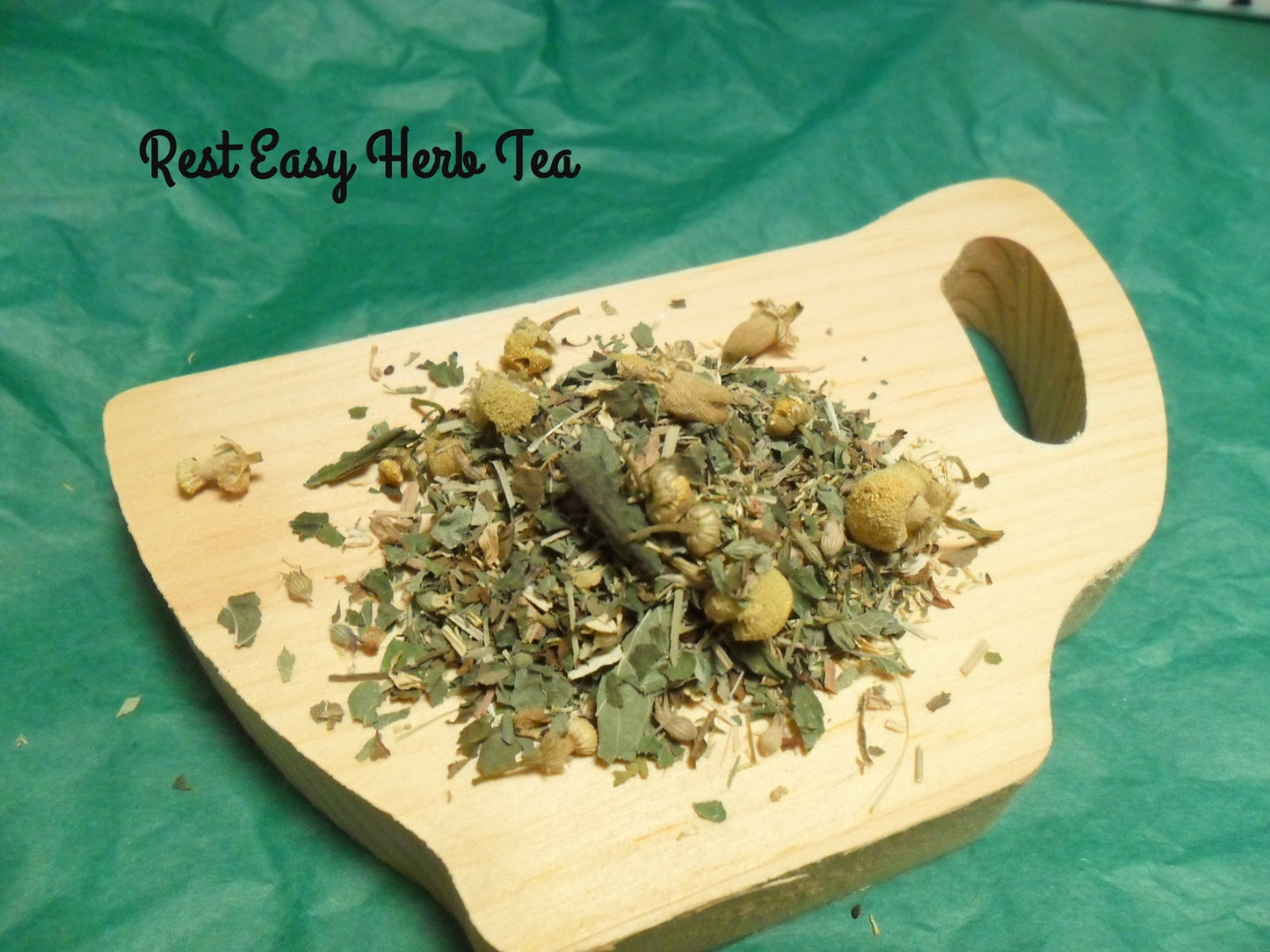 Loose Rest Easy Tea in a pile on wood tea cup containing chamomile, lemon balm, catnip, spearmint and lemon grass 