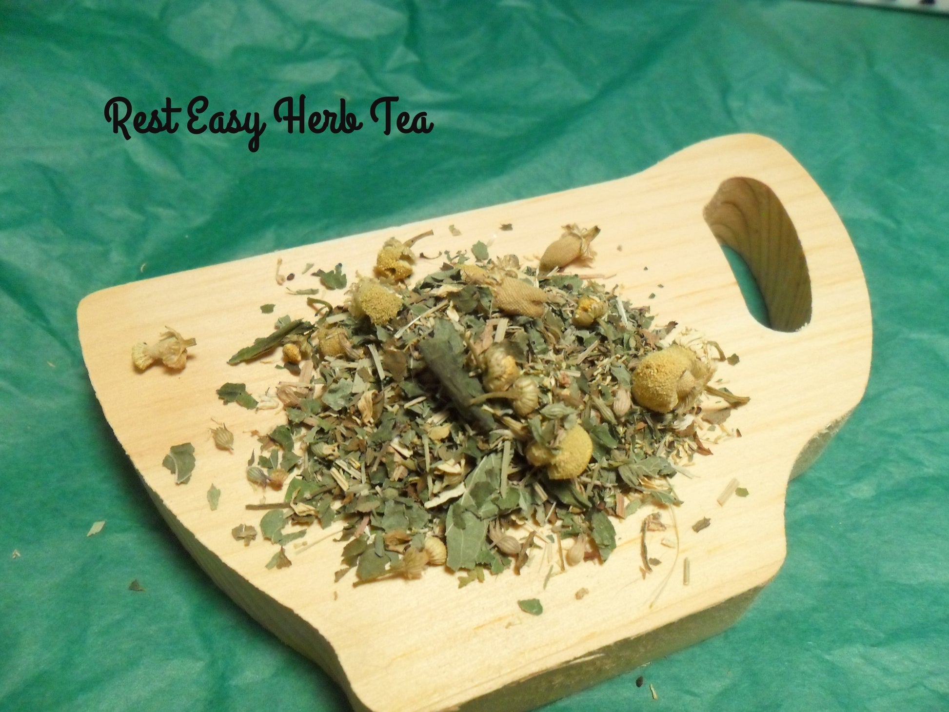 Loose Rest Easy Tea in a pile on wood tea cup containing chamomile, lemon balm, catnip, spearmint and lemon grass 